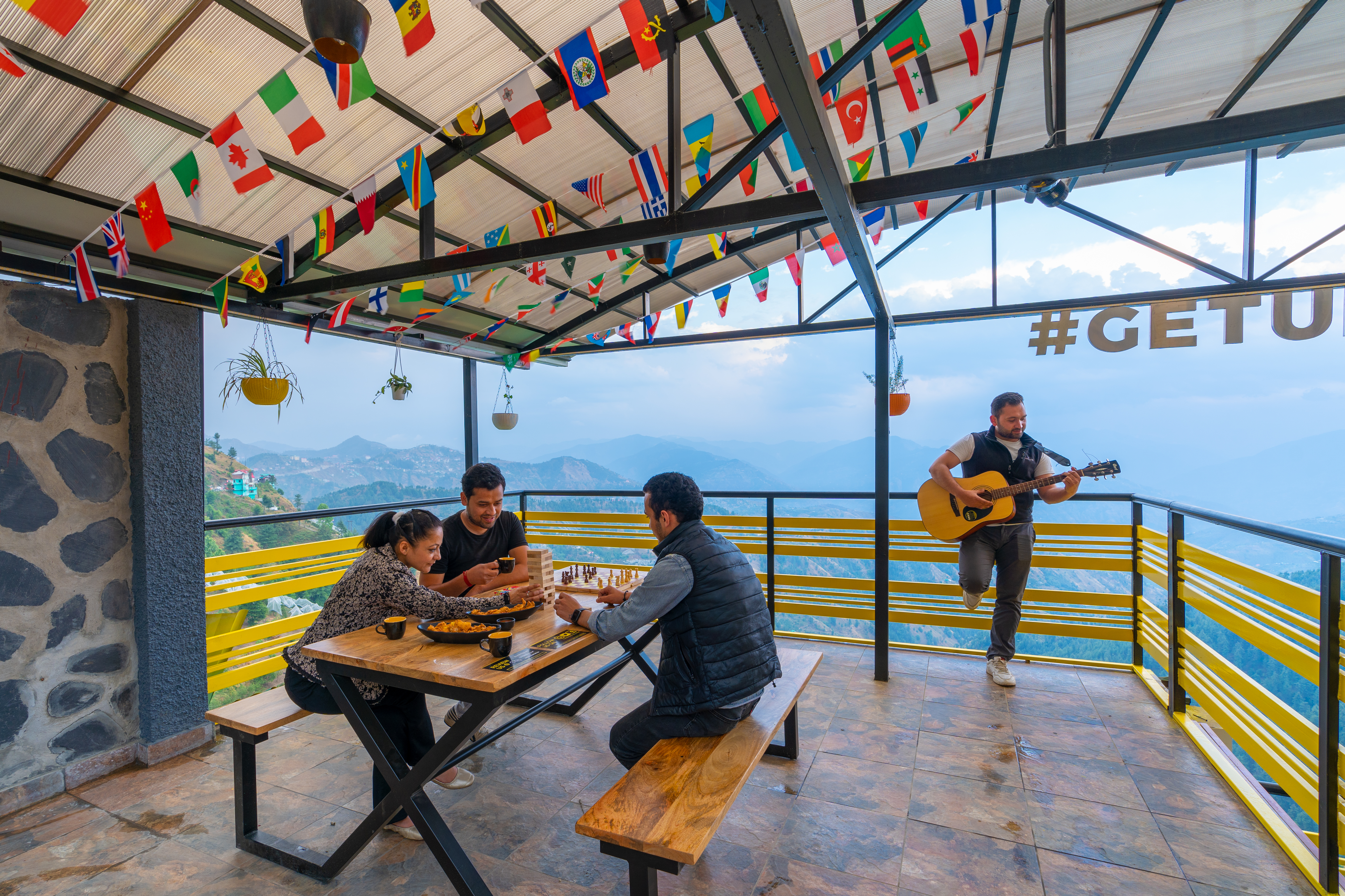 Travellers playing board games and guitar on a terrace with mountain views at The Hosteller