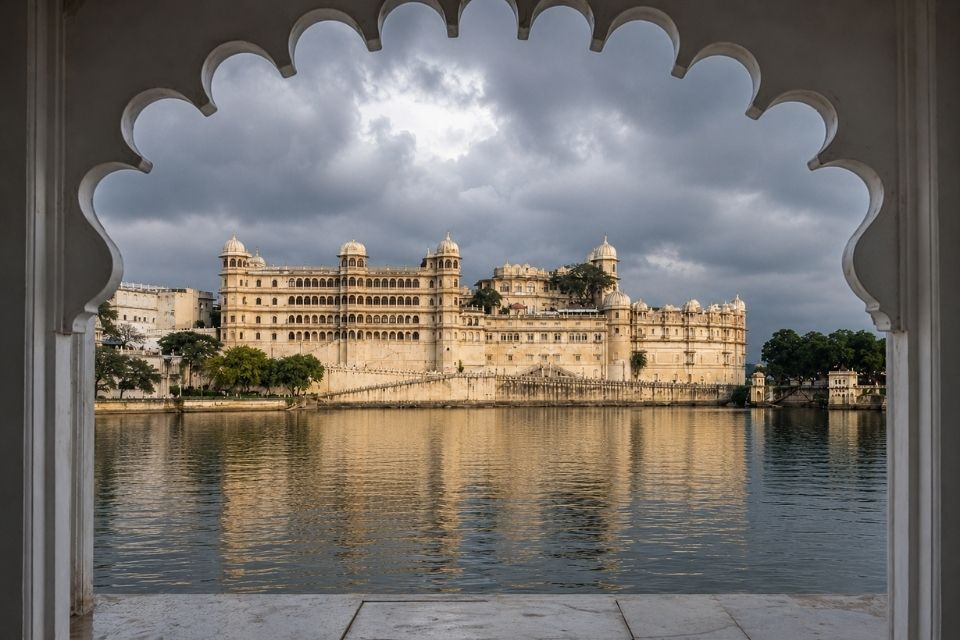 City Palace Udaipur framed through a scalloped stone archway under monsoon clouds